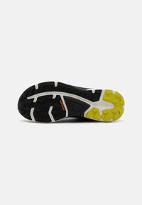 Suola di scarpe da trail running nera con distinti tasselli in gomma, accenti bianchi nella intersuola e sezioni gialle brillanti per aderenza e stabilità.