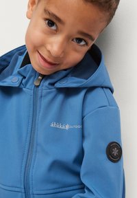 Blaue Outdoor-Jacke mit Reißverschluss, Druckknöpfen und Logodetail auf der Brust und dem Ärmel. Verfügt über eine Kapuze und eine glatte Textur.