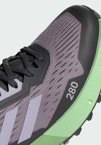 Scarpa da trail running grigia e nera con dettagli verdi. Presenta una tomaia in mesh traspirante, suola spessa e cinque strisce bianche. Numero '280' visualizzato.