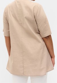 Beige tunic top made of lightweight fabric. Features short sleeves and a rounded hem. Simple, smooth texture with a loose fit.