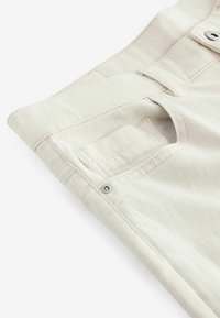 Off-white denimbyxor försiktigt vikta, med en bakficka, subtil struktur och en metallknapp som accent vid midjan.