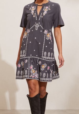 Robe gris foncé à manches courtes avec broderies florales et étoiles et col noué, portée avec des bottes hautes en suède noir.