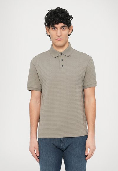 Poloshirt aus hellgrauem, strukturiertem Stoff mit drei Knöpfen und umgeschlagenem Kragen. Getragen mit blauen Jeans, ausgestattet mit kurzen Ärmeln und einer glatten Oberfläche.