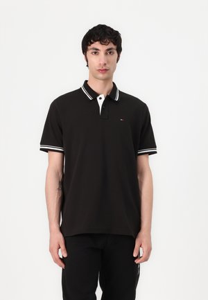 Čierna polo košeľa z bavlny, s bielym golierom členeným čiernymi pruhmi a malým logom na hrudi. Krátke rukávy, klasický strih.