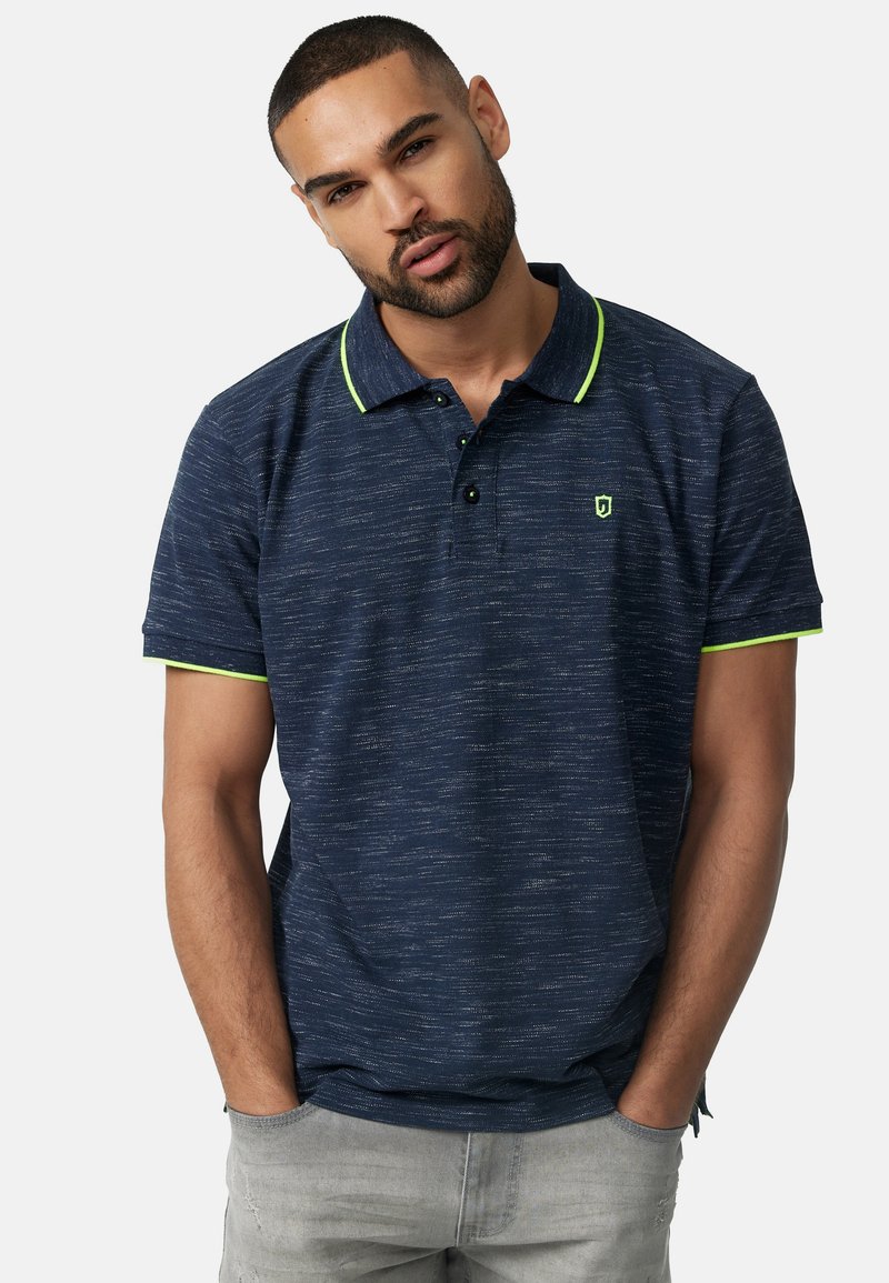 Marineblå polo skjorte med teksturert stoff, kontrasterende neongrønne detaljer på kragen og tre-knappers placket. Diskret logo på brystet.