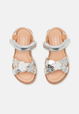 Zilveren sandalen met bloemige versieringen, voorzien van een band over de voet en een verstelbare enkelriem. Tan voetbed met stiksels.