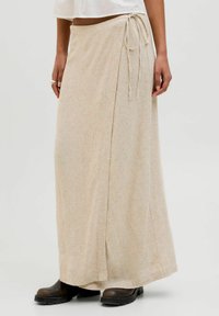 Bež dolg krilo iz mehke, teksturirane tkanine z božnim vezanjem. Ima tekočo silhueto in subtilen tkan vzorec.