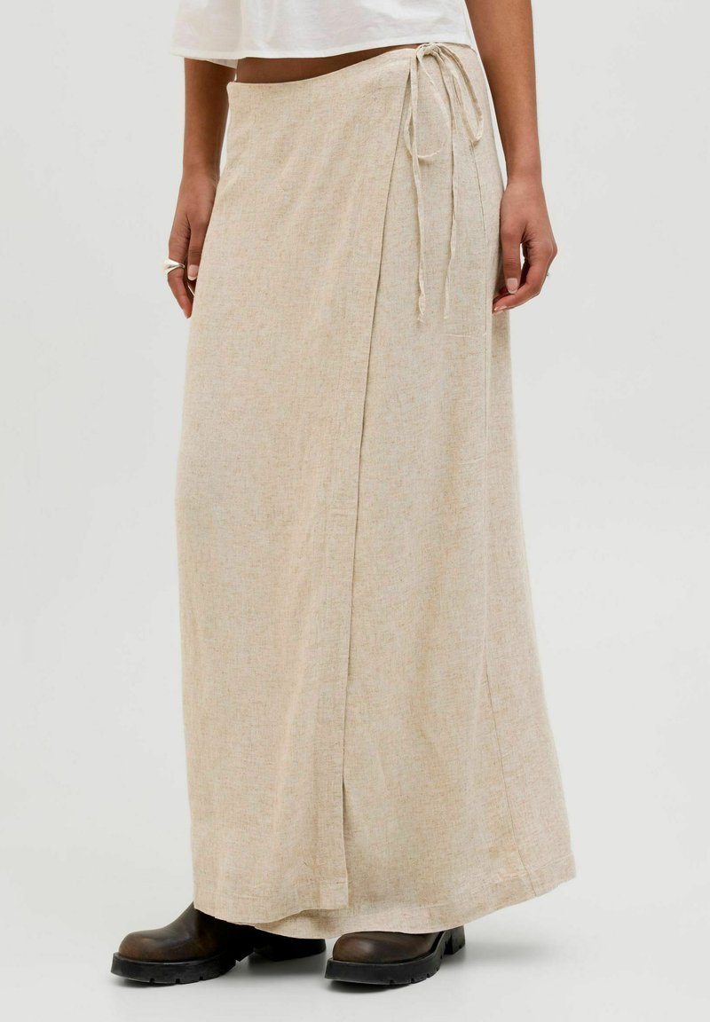 Bež dolg krilo iz mehke, teksturirane tkanine z božnim vezanjem. Ima tekočo silhueto in subtilen tkan vzorec.