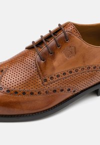 Scarpa da dress in pelle marrone perforata, con punta rotonda, lacci tonali, decorazioni brogue e piccoli accenti neri lungo il lato.