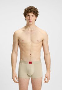 Slip beige con una cintura a logo rossa, caratterizzati da una vestibilità aderente e una superficie liscia, progettati per comfort e supporto.