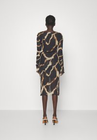 Robe à manches longues, cintrée, avec un motif tie-dye noir et beige. Présente des détails froncés et une longueur mi-mollet.