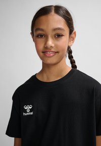 Camiseta de algodón negra con cuello redondo y mangas cortas, con un logo bordado en blanco en la parte izquierda del pecho.