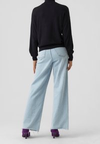 Suéter de punto negro combinado con jeans azul claro de pierna ancha. Cuenta con dobladillo deshilachado y dos bolsillos traseros. Se lleva con zapatos de tacón alto morados.