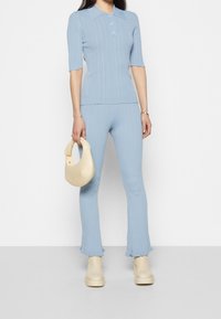 Haut en tricot côtelé bleu clair à manches courtes avec patte de boutonnage à trois boutons, associé à un pantalon évasé côtelé assorti et un sac à main crème.