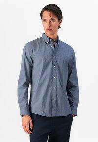 Camisa de botones azul con estampado, hecha de algodón. Presenta un collar, mangas largas y una tapeta frontal con botones blancos. Logotipo en el pecho.