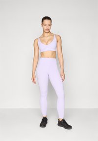 Light lavender sports bra and leggings set, featuring a smooth texture, close-fitting design, and black athletic shoes.