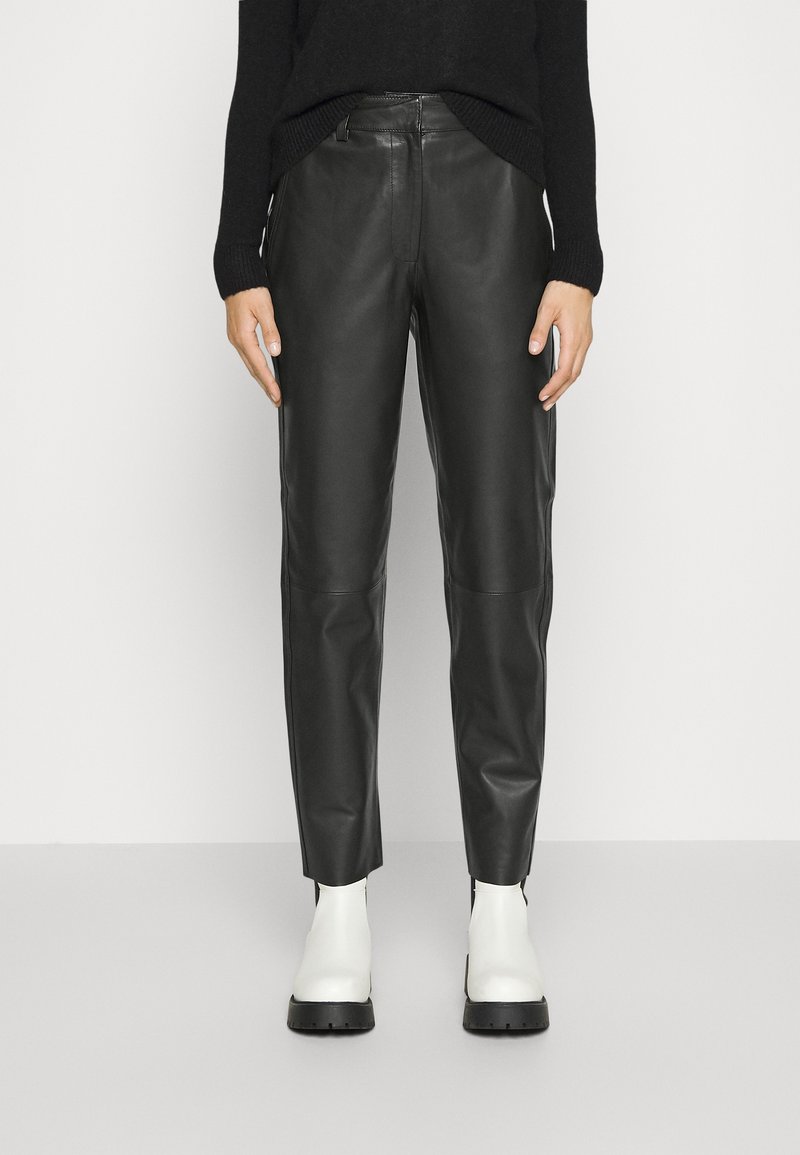 Black leather pants with a tapered fit, featuring a smooth texture and front zipper. Paired with white ankle boots with thick black soles.