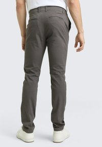 Γκρι βαμβακερό παντελόνι με στενή εφαρμογή, δύο πίσω τσέπες και ρεβέρ στα μπατζάκια, συνδυασμένο με λευκά αθλητικά παπούτσια σε ουδέτερο φόντο.