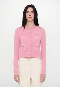 Cardigan court rose en tricot texturé, avec deux poches plaquées, fermeture à boutons sur le devant, et bords côtelés aux poignets et à l'ourlet.