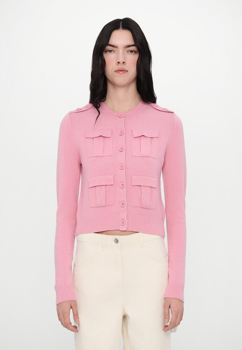 Cardigan court rose en tricot texturé, avec deux poches plaquées, fermeture à boutons sur le devant, et bords côtelés aux poignets et à l'ourlet.