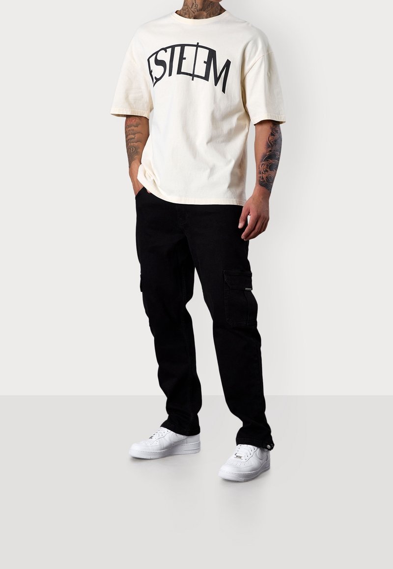 Cream cotton t-shirt with black "ESTEEM" print, paired with black cargo pants featuring side pockets and white sneakers.