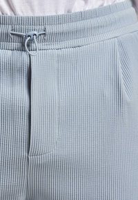 Pantalones de canalé azul claro con cintura ajustable y bolsillos frontales, con una tela texturizada y un ajuste relajado.