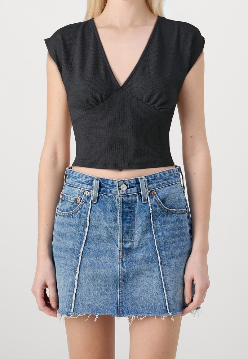 Top court noir en tissu froissé avec manches courtes, associé à une jupe mini en denim bleu avec un ourlet effiloché et des coutures avant.