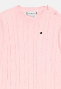 Svetlorožový pletený sveter pre bábätká s dvoma gombíkmi na ramene a malou vyšívanou logom Tommy Hilfiger na prednej strane.