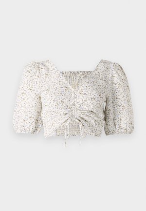 Blouse blanche à manches courtes avec imprimé floral beige et bleu. Présente un devant smocké et un décolleté carré avec des cordons de serrage.