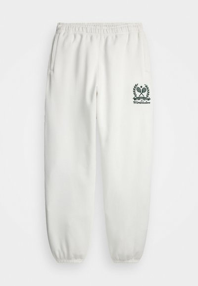 Bele hlače s elastičnim pasom, stranskimi žepi in zoženimi manšetami. Imajo zeleno vezeno logo Wimbledona na levem hlačniku.