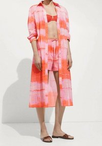 Rosa und orangefarbener Batik-Chemisierkleid mit langen Ärmeln, leichtem Stoff, Knopfverschluss und lockerer Passform, über einem passenden Bikini getragen.
