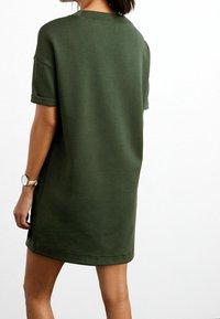 Robe T-shirt verte olive à manches courtes, avec une coupe décontractée, un col rond et des manches retroussées, fabriquée en tissu doux en mélange de coton.