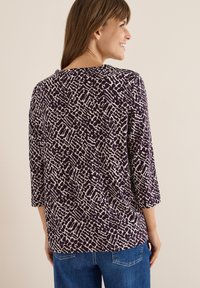 Lila mönstrad topp med 3/4 ärmar, som har abstrakta vita mönster. Mjuk tyg, avslappnad passform, kombinerad med denimbyxor.