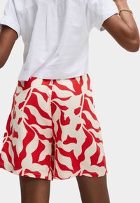 Rote und cremefarbene Shorts mit einem wellenförmigen Muster aus leichtem Stoff, von hinten mit einem schlichten weißen Oberteil präsentiert.