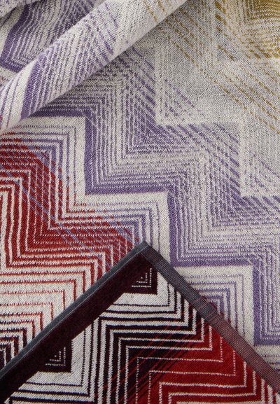 Tissu texturé avec des motifs géométriques en zigzag violet, rouge, moutarde et noir sur fond crème, plié pour montrer le devant et le dos.