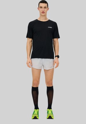 Black short-sleeve sports shirt, light gray shorts, knee-high black compression socks, and green shoes; minimalistic design, breathable fabric.