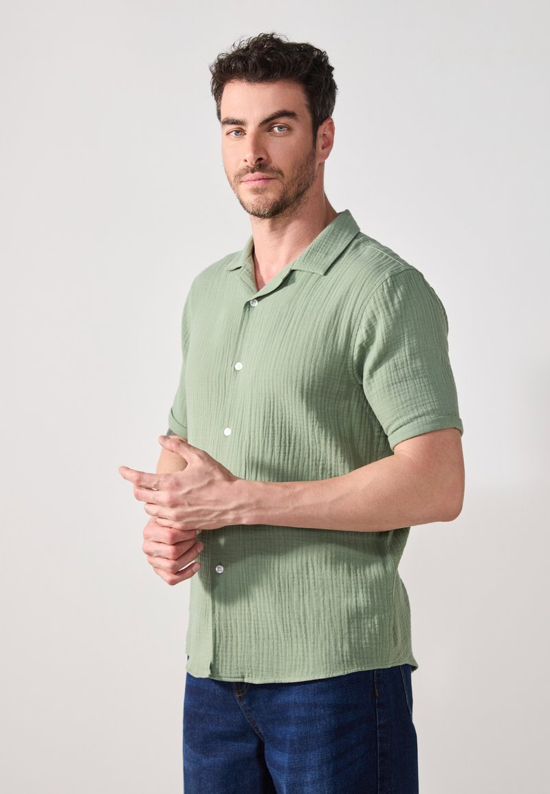 Lichtgroen shirt met korte mouwen van textuurstof, met knoopsluiting en een campagnekraag, gecombineerd met blauwe spijkerbroek.