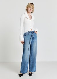 Cardigan bianco a coste con colletto e polsini in pelliccia sintetica, abbinato a jeans blu a vita alta e gamba larga e ballerine nere a punta.