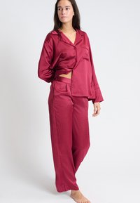 Bordeaux satijnen pyjamapak bestaande uit een knoopblouse met zakken en lange broek, beide met een subtiel gestippeld patroon en een ontspannen pasvorm.