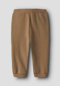 Ruskeat, ribbineulotut housut, joissa on kapenevat lahkeet ja joustava vyötärönauha. Housuissa on sivutaskut ja nilkkureunukset.