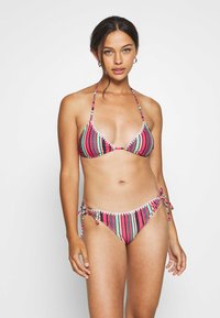 Costume da bagno a righe con top triangolare e parte inferiore con laccetti. I colori includono rosa, blu e bianco. Realizzato in tessuto morbido con finitura testurizzata.