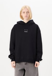 Black hooded sweatshirt with a loose fit, featuring white text “C P H STUDIOS” on the front. Soft fabric with ribbed cuffs and hem.