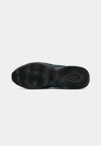 Potplat crne i tamnozelene tenisice prikazuje teksturirane uzorke za bolje prianjanje i "Airmax" logo na području pete.