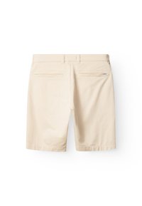 Bež pamučne kratke hlače glatke teksture. Imaju dva stražnja džepa s horizontalnim šavovima i malu naljepnicu marke na desnom džepu.