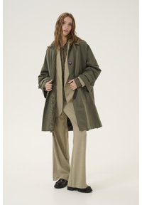 Oliivroheline oversized trench-kate kergest kangast, suured nööbid, laiad varrukad ja sile sisevooder, kantud sobiva kostüümi peal.