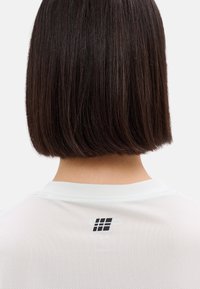 White mesh sports shirt featuring a rounded collar and a small black logo at the back, showcasing a breathable, lightweight texture.