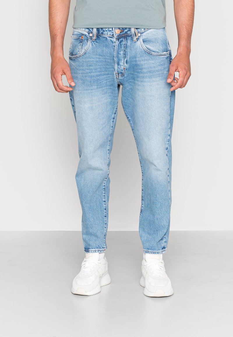 Jasnoniebieskie dżinsy z denimu o prostych nogawkach, z pięcioma kieszeniami i subtelnym przetarciem. Wykończone zapięciem na guziki oraz kontrastującymi szwami.