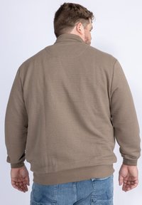 Hnědá žebrovaná mikina s vysokým límcem, elastickými manžetami a spodním lemem. Tkanina vypadá měkce a strukturovaně, navržena pro teplo a pohodlí.