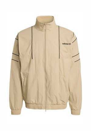 Veste beige zippée avec un col montant, des bandes latérales noires, des poignets élastiques, et le logo Adidas sur la poitrine. Fabriquée en matière légère.
