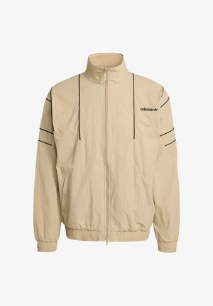 Smėlio spalvos striukė su užtrauktuku, aukšta apykakle, juodomis šoninėmis juostelėmis, elastinėmis rankogalių dalimis ir „Adidas“ logotipu ant krūtinės. Pagaminta iš lengvos medžiagos.